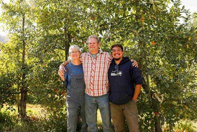 3 apple farmers stand in front of apple trees.