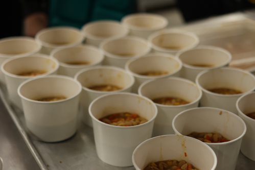 Tray containing approximately 20 paper bowls containing white bean chili.