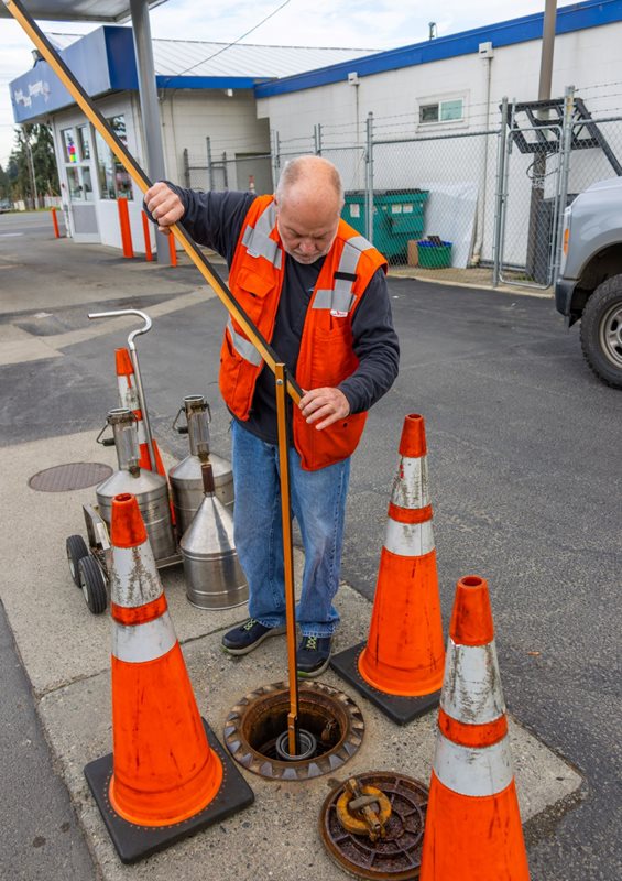 man inserting measuring stick into underground fuel tank