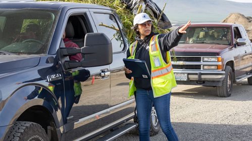pickups in line to drop off yard waste and woman in safety vest pointing