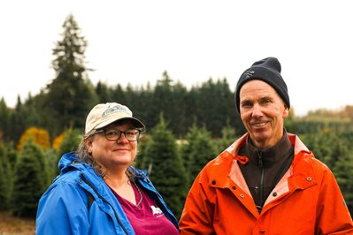Christmas tree growers stand in row of trees.