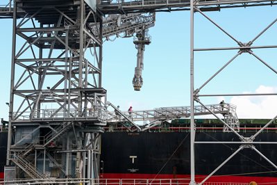 Metal crane hovers above black and red cargo ship.